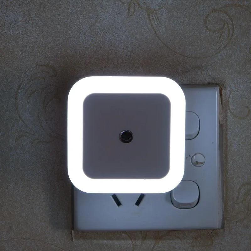 Square night light attached to a wall socket with a floral patterned wallpaper background.