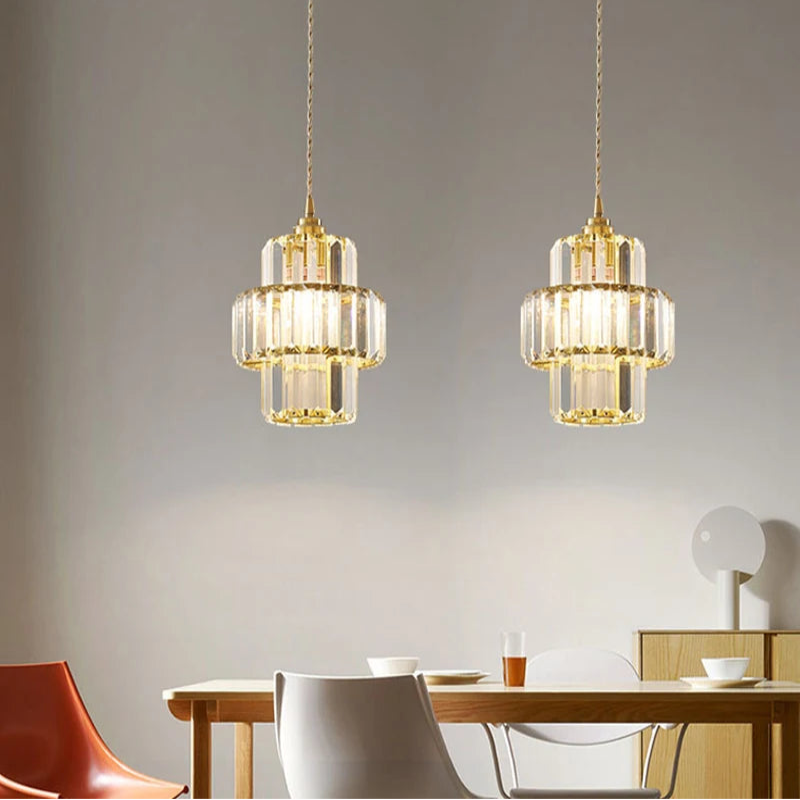 Two gold pendant lights hanging above a dining table with chairs.
