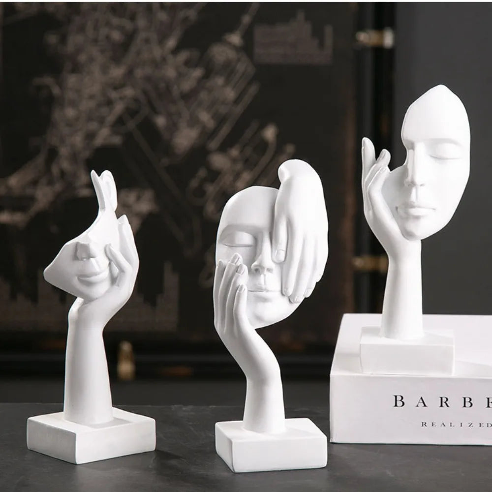 Three white abstract sculpture figurines on a dark surface with a blurred background.