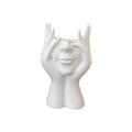 White ceramic vase shaped like a face with hands on a white background