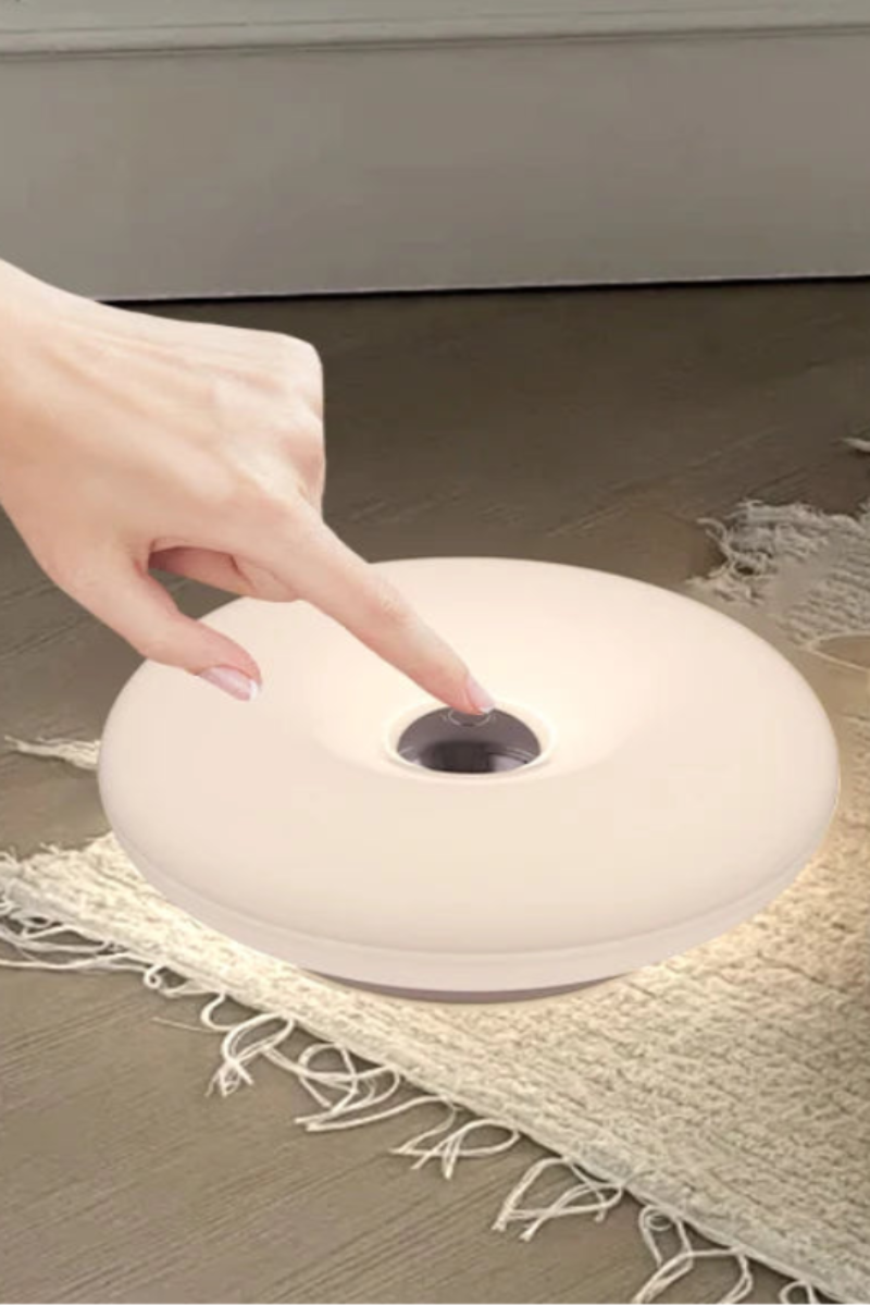 A round white touch switch light on a frayed cream rug next to a white tote bag, with a hand pressing the center button. Text overlay reads 'Touch switch'.