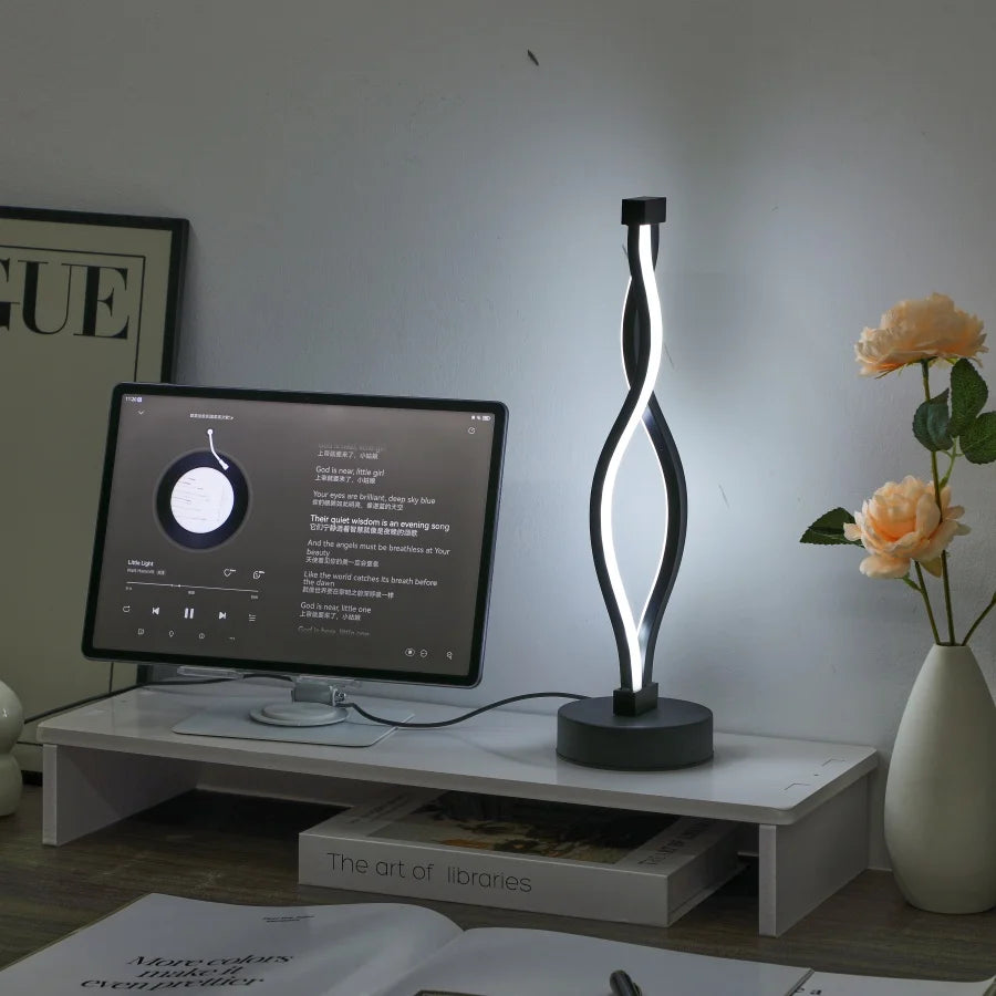 Modern desk setup with a computer monitor, lamp, and flowers on a white surface.