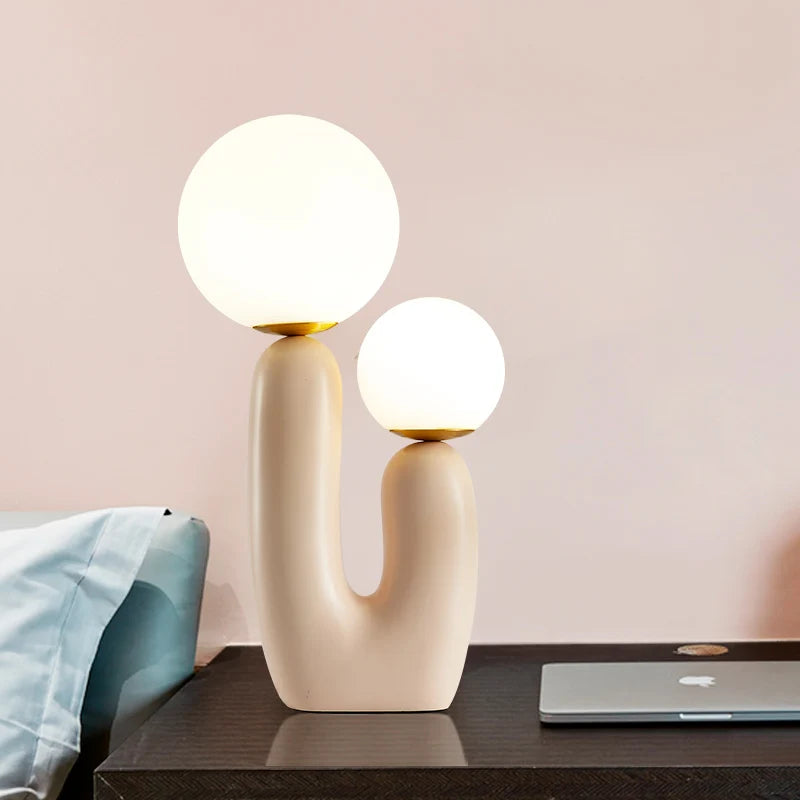 Modern table lamp with two round lights on a desk against a pink wall.