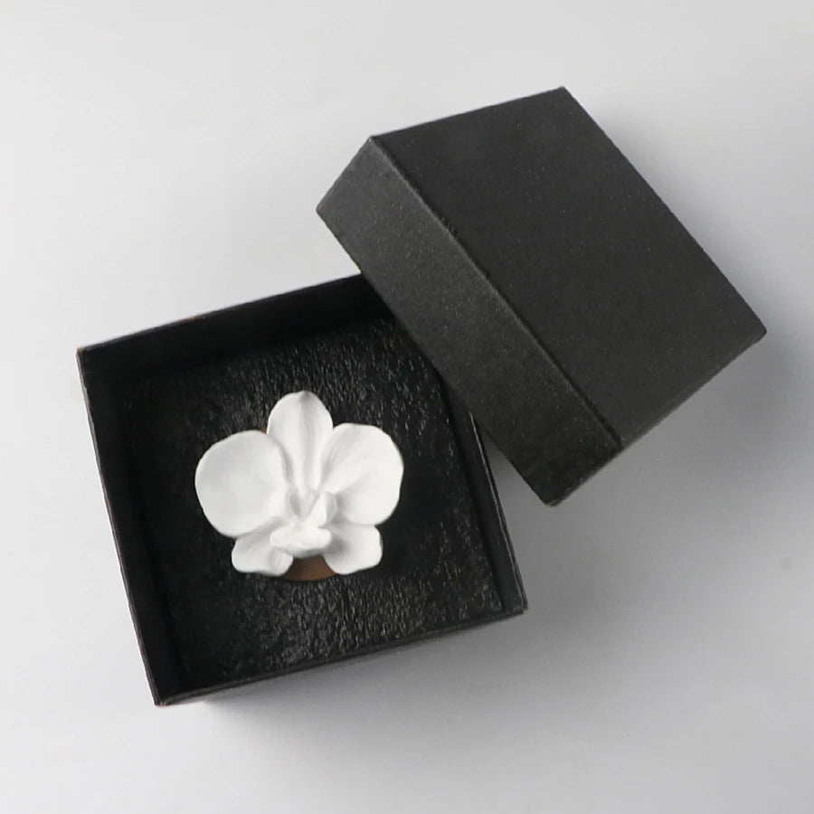 White orchid-shaped object in an open black box on a light gray background