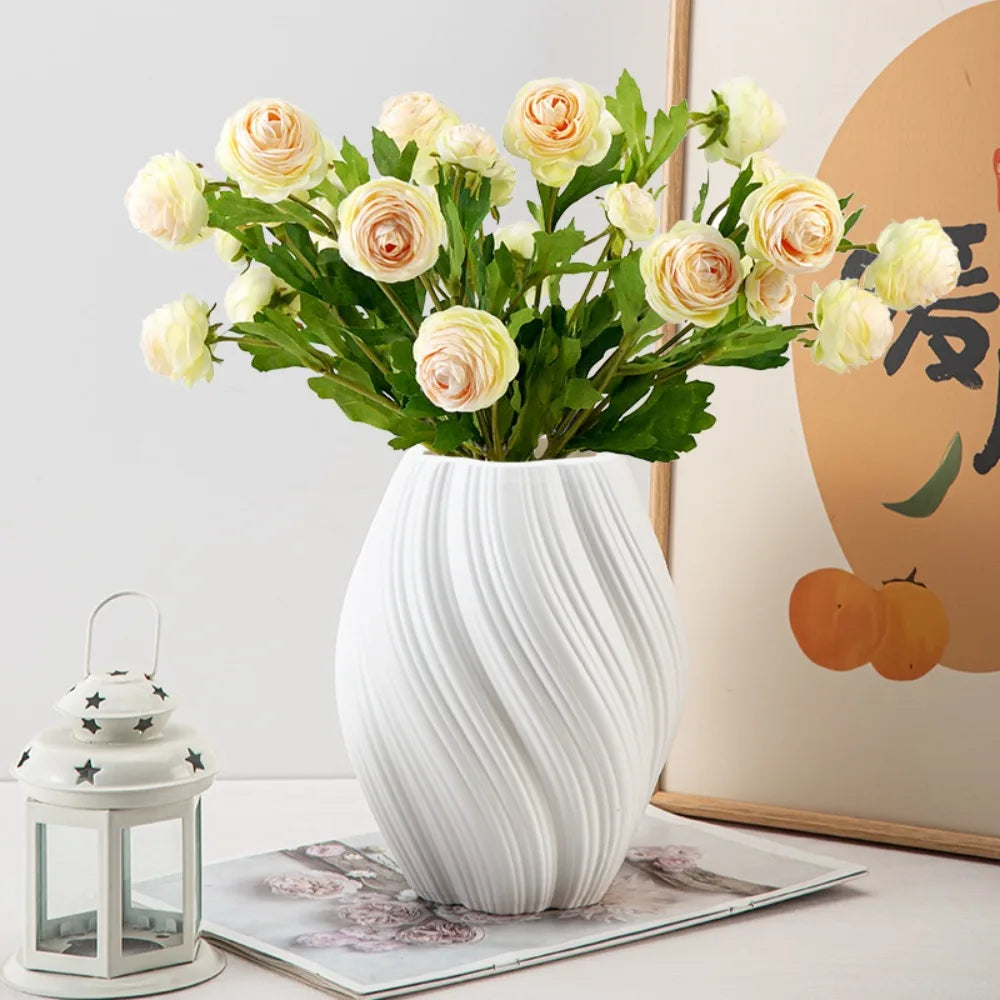 White vase with yellow flowers on a table next to a lantern and magazine