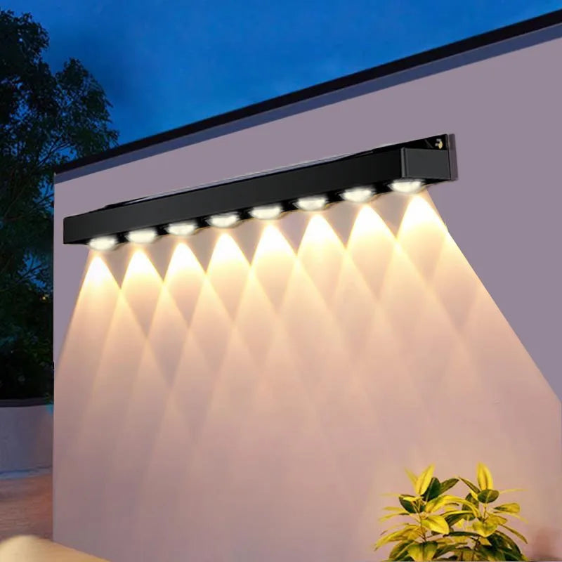 Outdoor wall light fixture on a building exterior with a plant in the foreground.