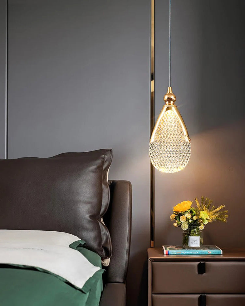 Decorative pendant light hanging above a bed with a side table and flowers.