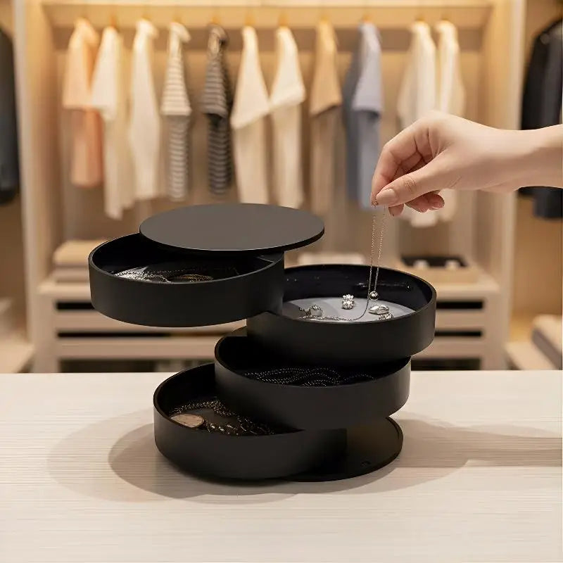 Black three-tiered jewelry organizer with a hand placing an earring inside, set against a blurred background of clothes on hangers.
