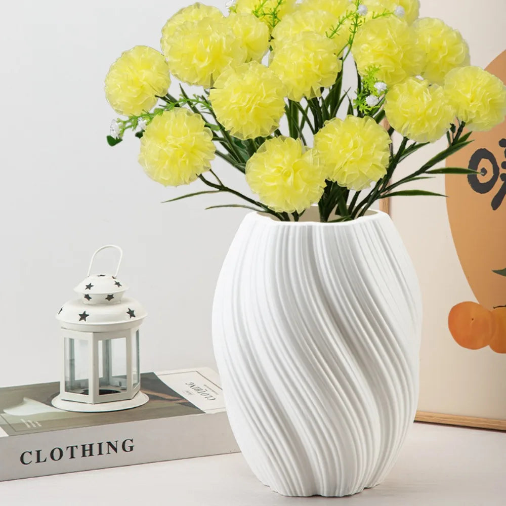 White textured vase with yellow flowers on a surface with books and a lantern.