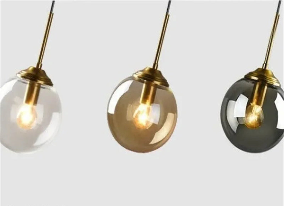 Three pendant lights in transparent, amber, and smoky gray with gold fixtures on a white background.