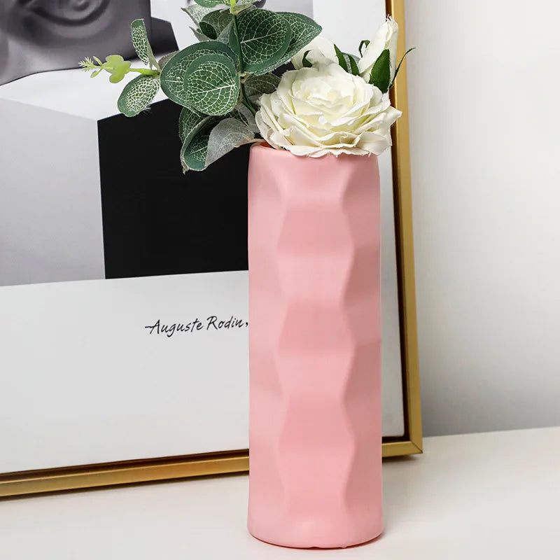 Pink vase with white flowers and green leaves on a white surface