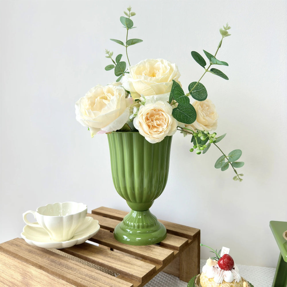 Green vase with white flowers on a wooden table against a white background