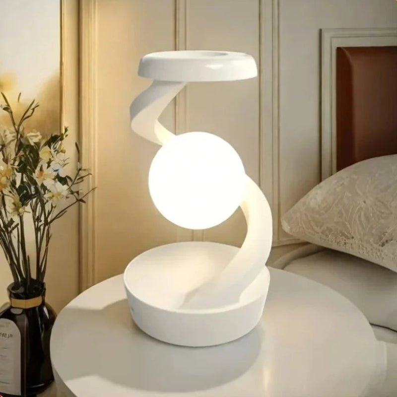 A modern white spiral-shaped table lamp with a glowing spherical bulb, displayed on a white round table in a bedroom setting.