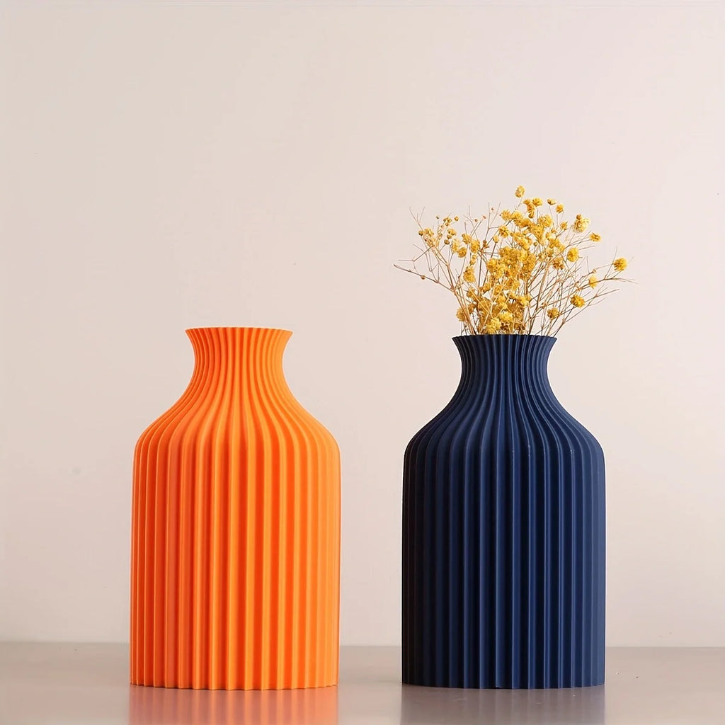 Two ribbed ceramic vases on a light gray surface against a warm off-white background. The left vase is bright orange, and the right vase is dark blue, holding a small arrangement of yellow dried flowers.