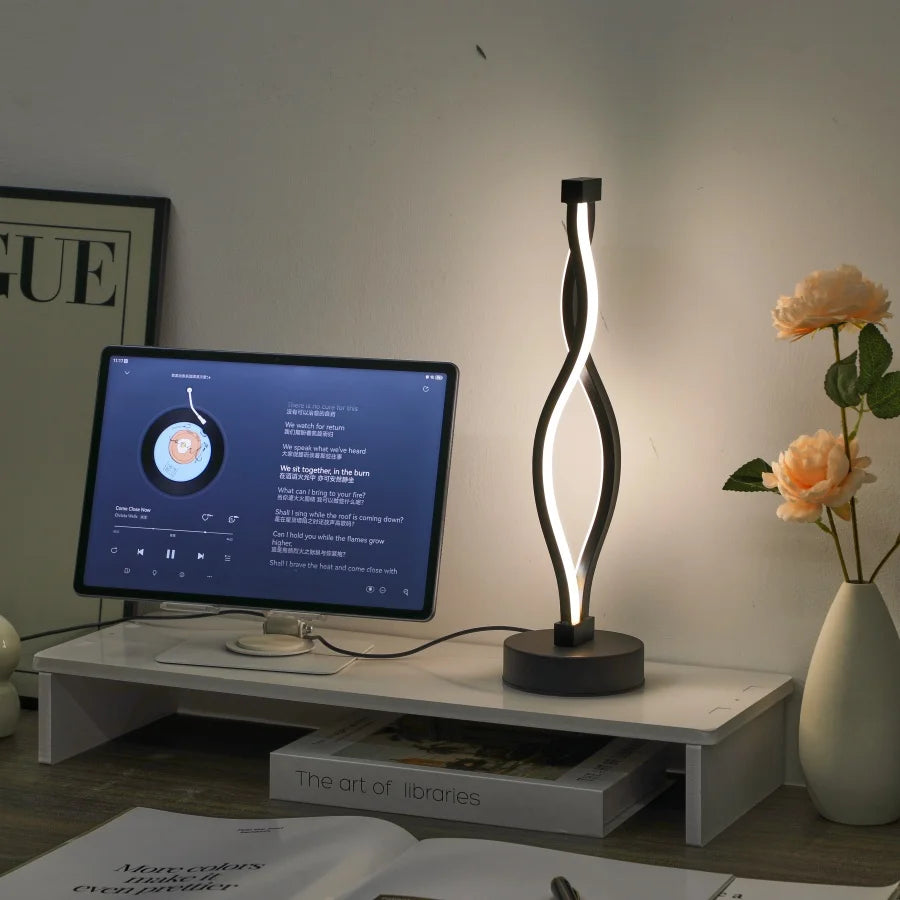 Modern desk setup with a computer monitor, lamp, and flowers on a wooden surface.