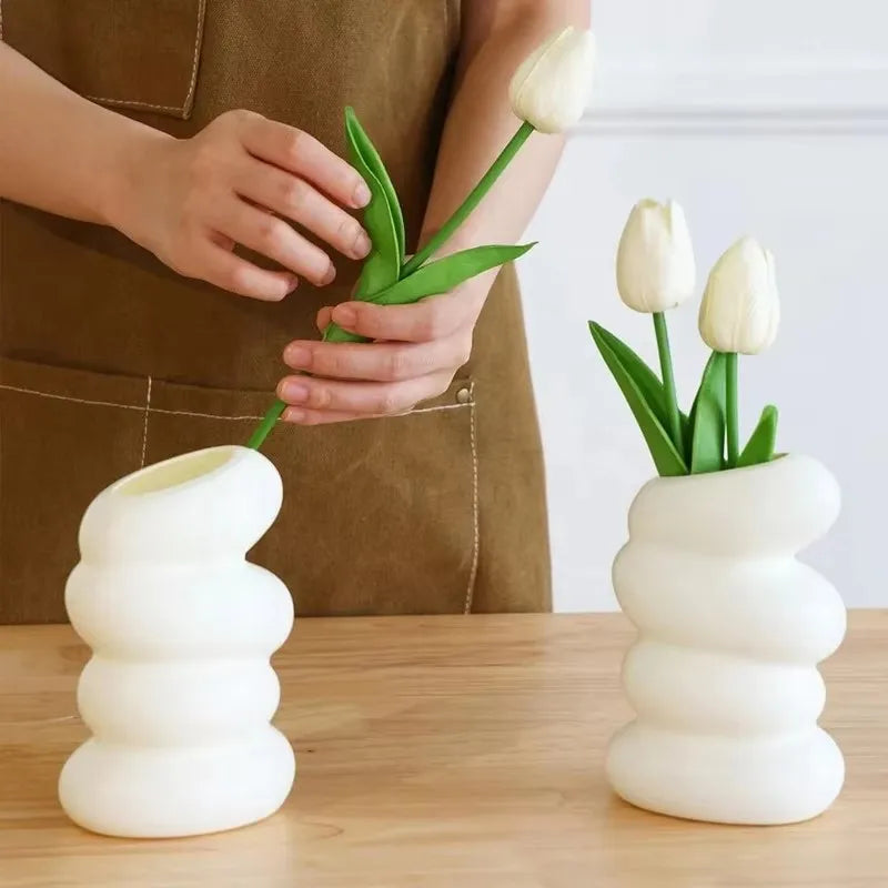 Person arranging tulips into ribbed white vases on a wooden surface.