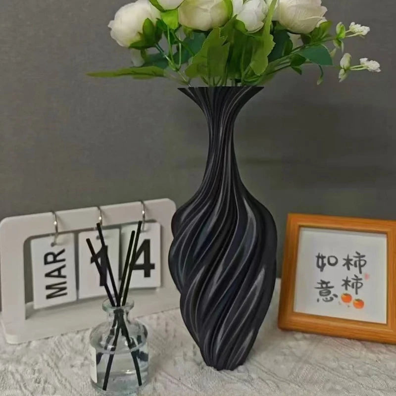 Black textured vase with white flowers on a gray surface, with a calendar and decorative frame in the background.