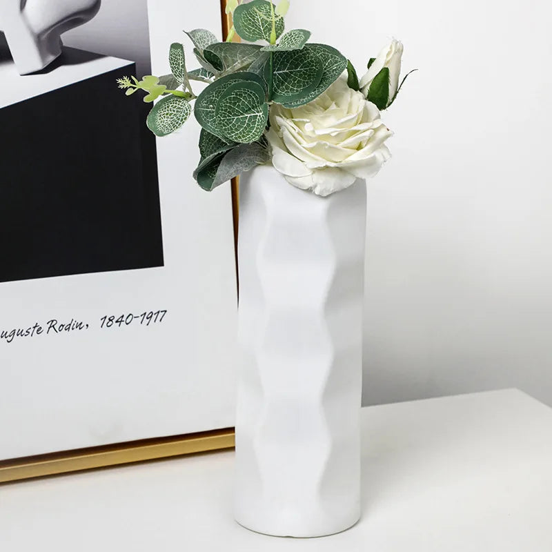 White vase with green leaves and white flowers on a white surface