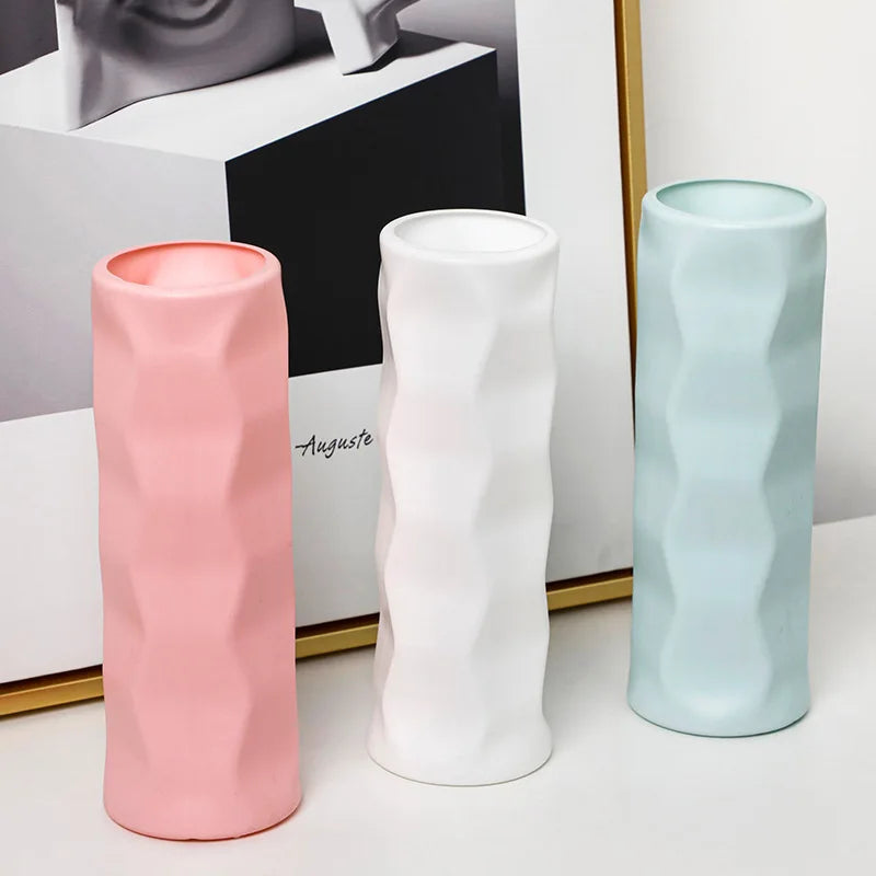 Three ceramic vases in pink, white, and light blue on a white surface with a blurred background.