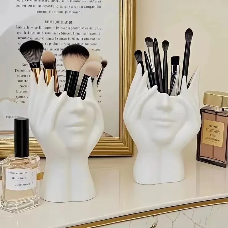 White hand-shaped brush holders with makeup brushes on a vanity table.