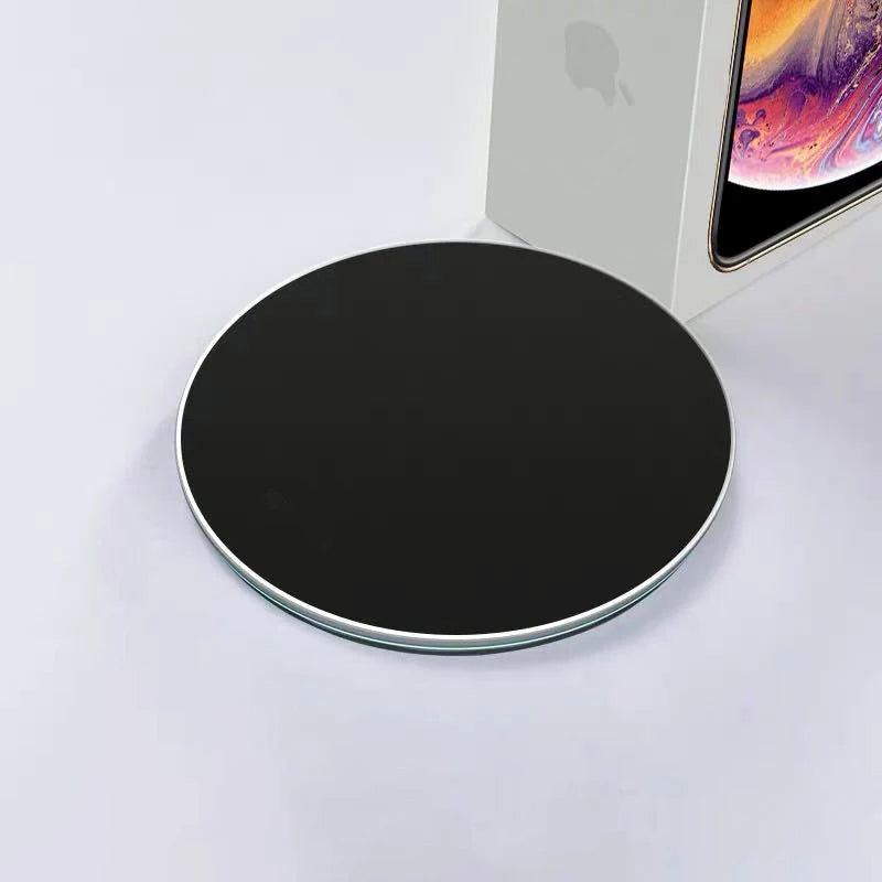 Black wireless charging pad on a white surface with an iPhone in the background