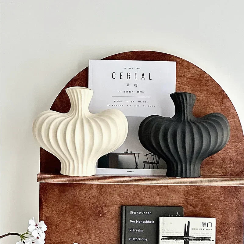 Two ribbed ceramic vases, one cream white and one matte black, displayed on a wooden shelf with books in the background.