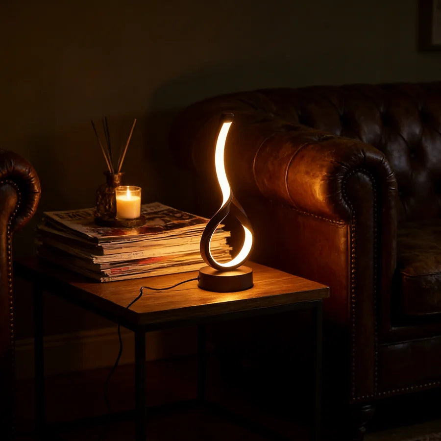 Decorative table lamp on a wooden side table with a candle and books, in a dimly lit room.