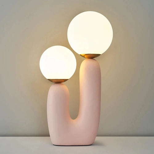 Modern table lamp with two spherical lights on a pink base against a neutral background