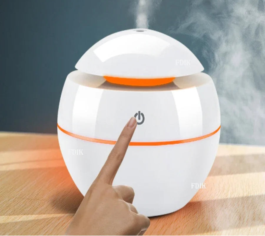 White and orange humidifier with steam being emitted, being touched by a hand on a wooden surface.