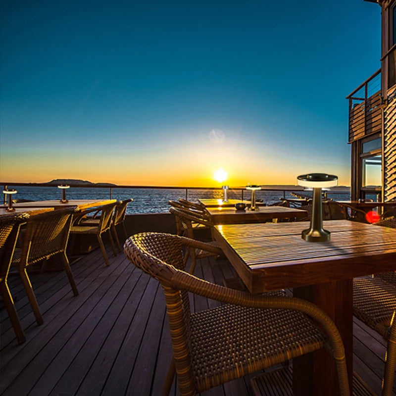 Sunset over a waterfront with wooden tables and chairs on a deck.