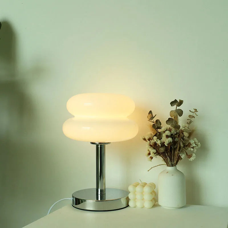Table lamp with a vase of dried flowers and a candle on a surface against a light green wall.
