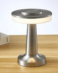 Metallic lamp on a wooden surface with a plant and book in the background