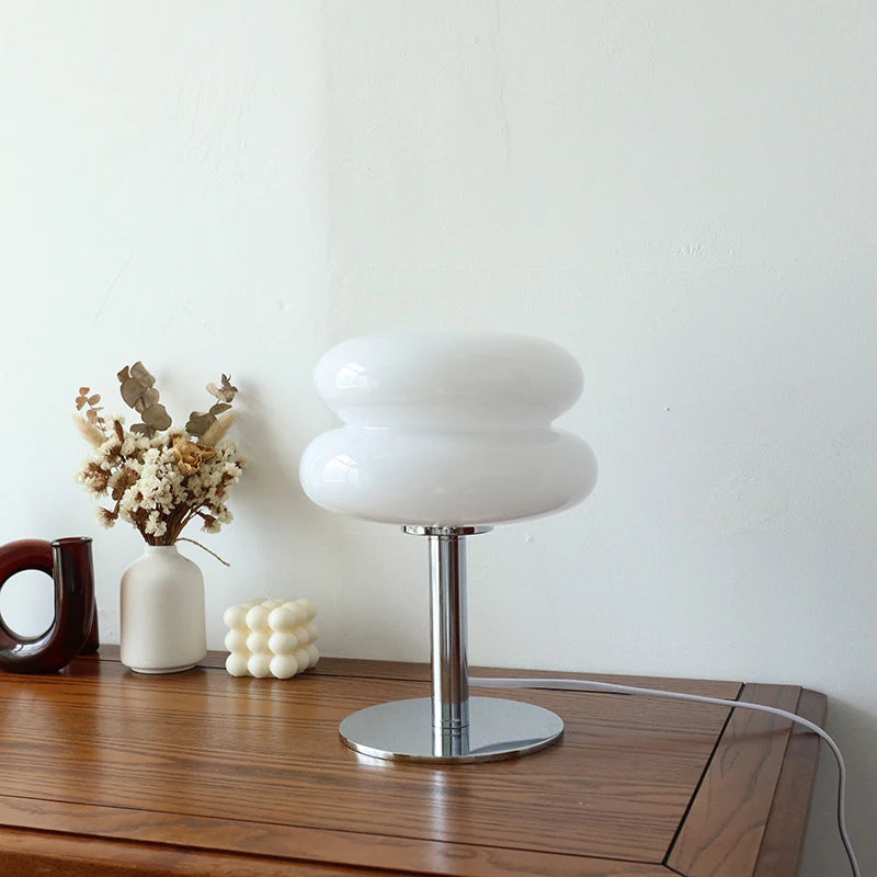 White table lamp on a wooden surface with decorative items against a plain wall.