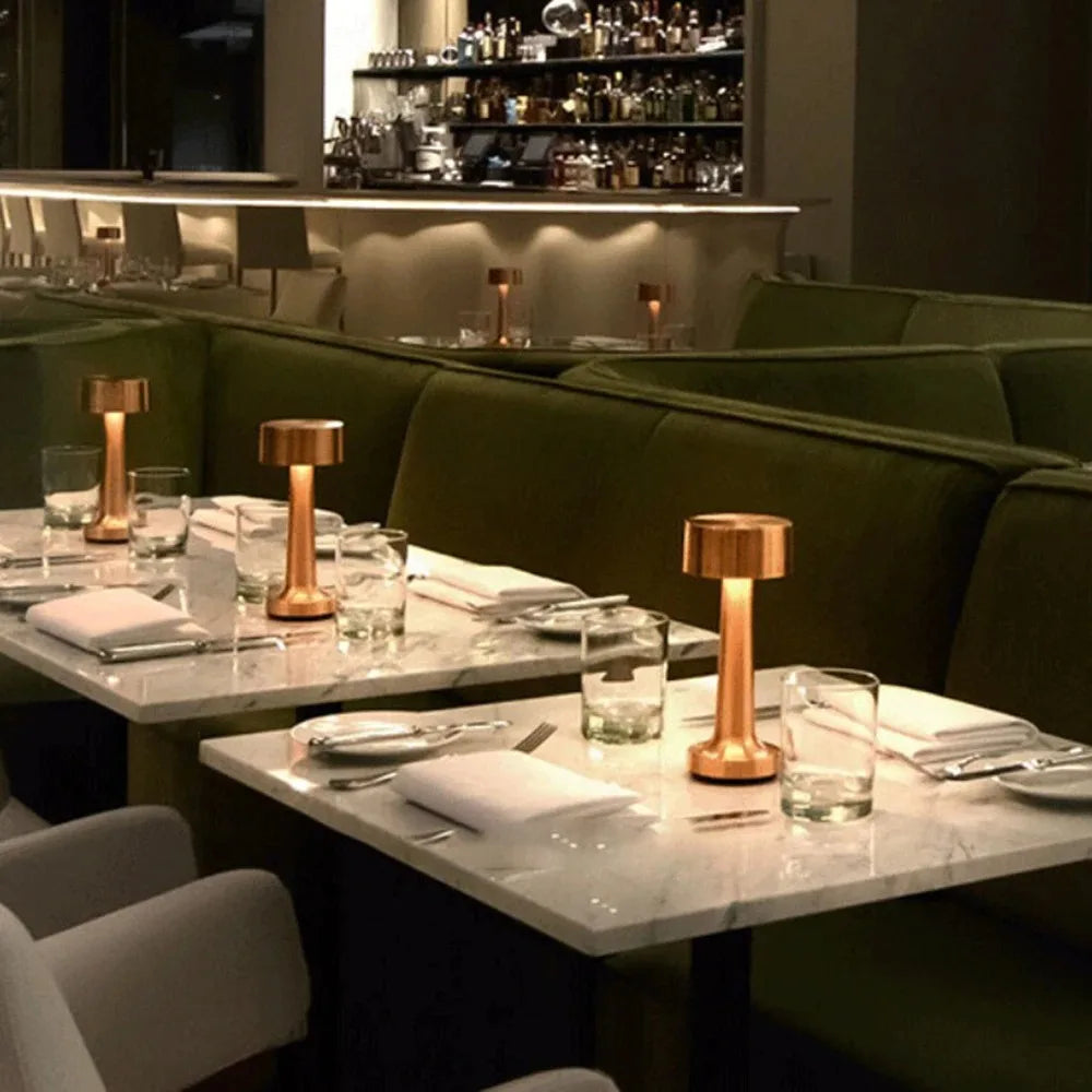 Dining area with marble tables, green booths, and copper lamps in a dimly lit restaurant.