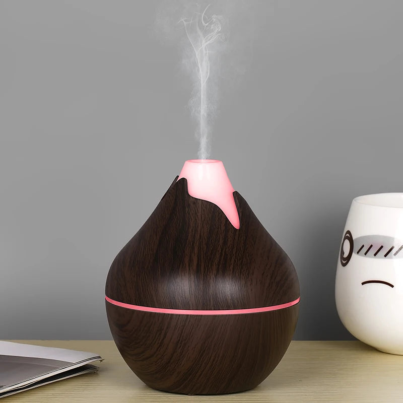 Wooden essential oil diffuser with pink accents emitting steam on a wooden surface.