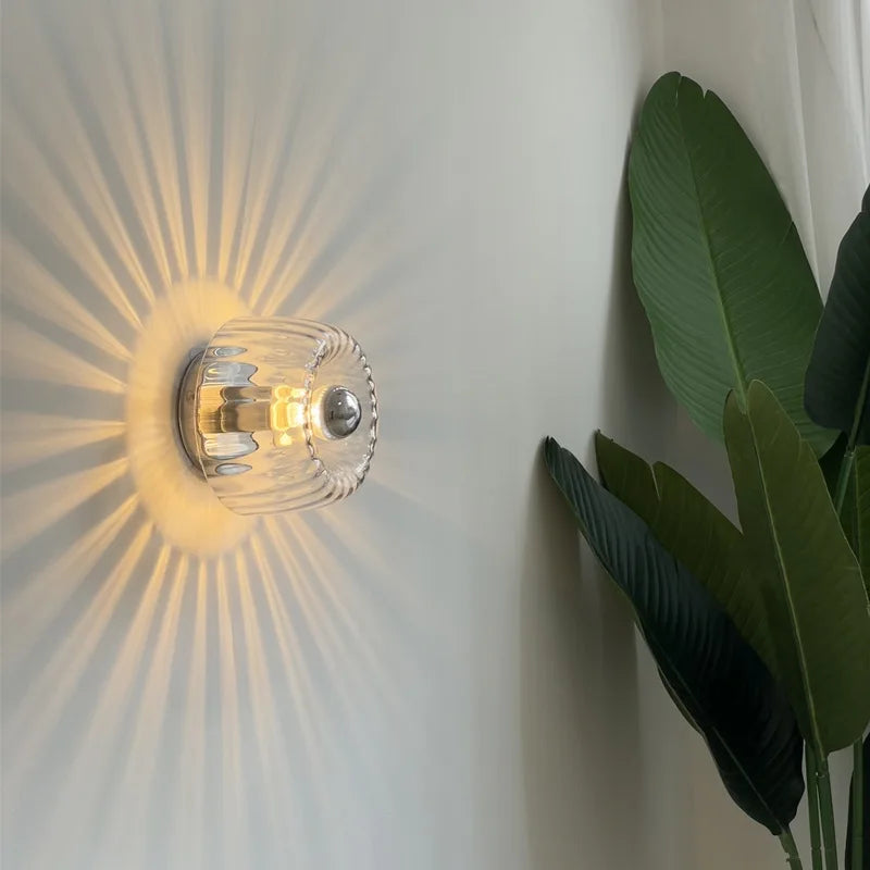 Wall-mounted light fixture with a glass shade casting a warm glow on a wall, accompanied by a plant.