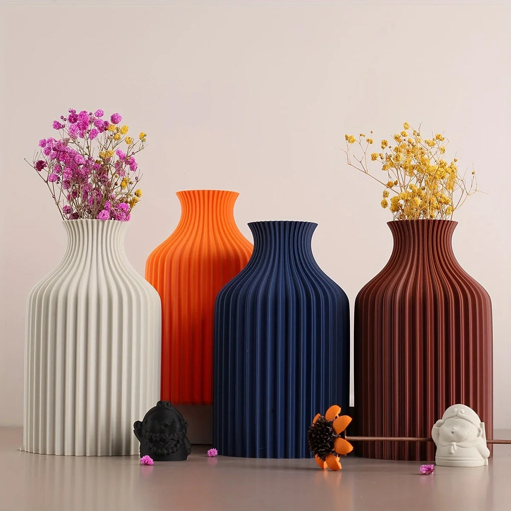 Four ribbed ceramic vases in white, orange, navy blue, and reddish-brown, arranged on a tabletop with dried flowers in each vase against a plain light beige background.
