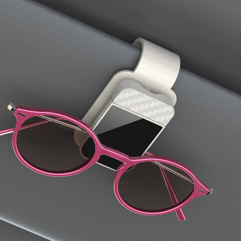 Pink sunglasses hanging from a car visor holder on a gray car interior.