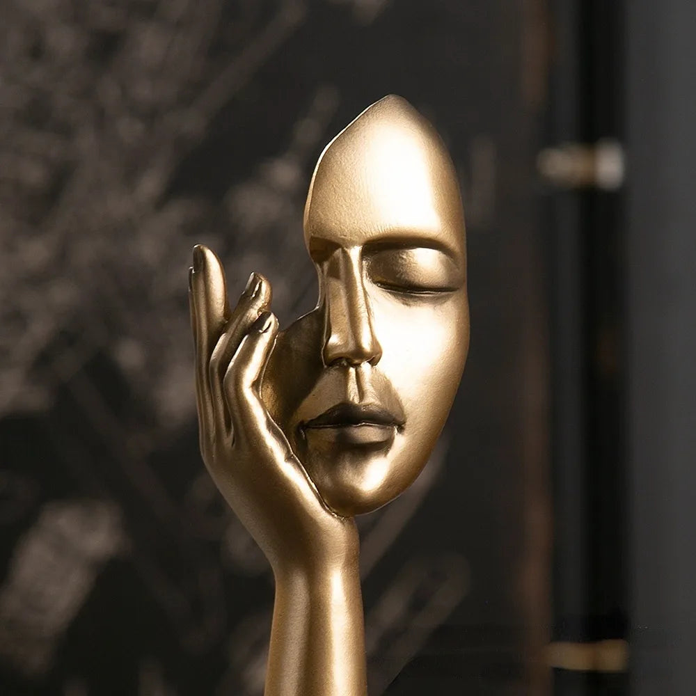 Gold sculpture of a hand holding a face against a dark background