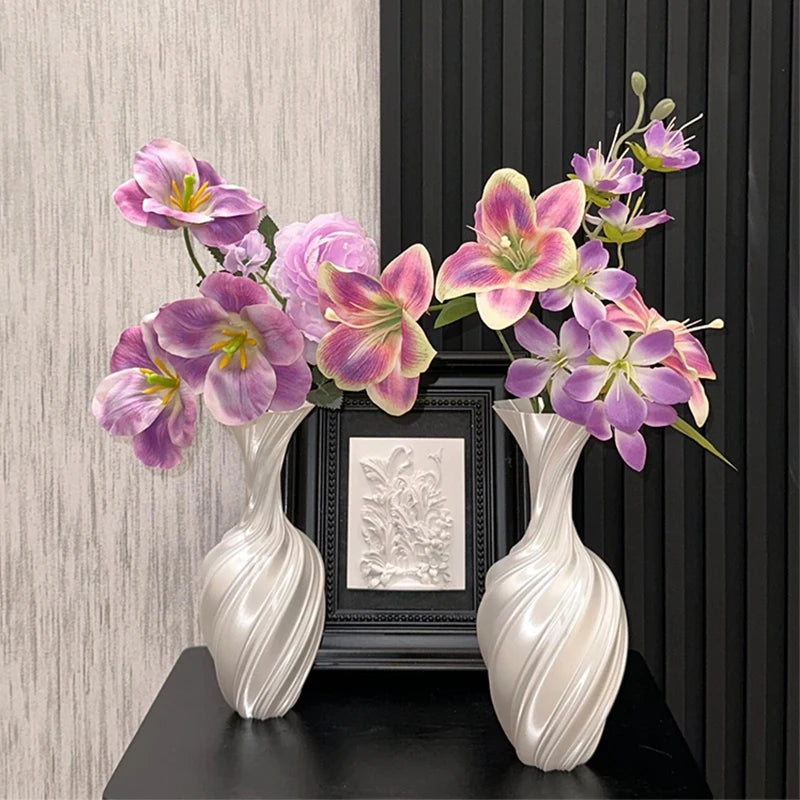 Two white vases with pink and purple flowers on a black surface against a striped wall.