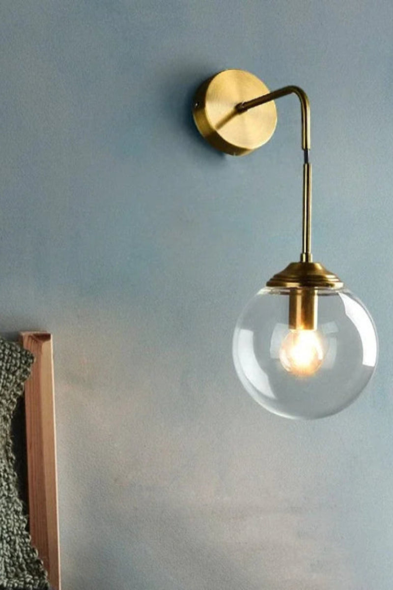 Wall-mounted lamp with a clear glass shade and gold fixture on a light blue wall.