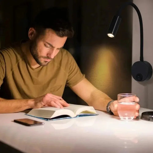 Man reading a book at a desk with a lamp and glass of water