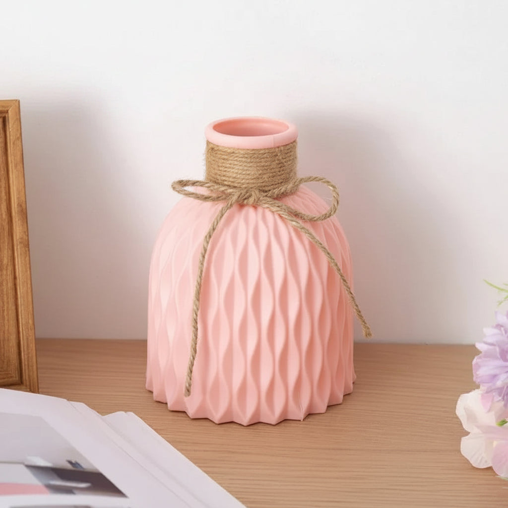 Pink ceramic vase with textured design and twine bow on a wooden surface.