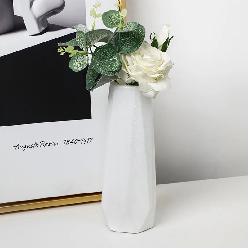 White vase with flowers on a table next to a framed picture
