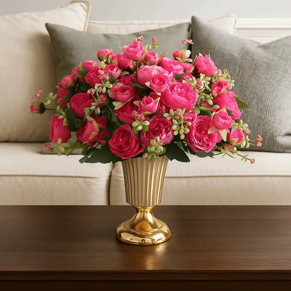 Bouquet of pink flowers in a gold vase on a wooden table with a couch in the background