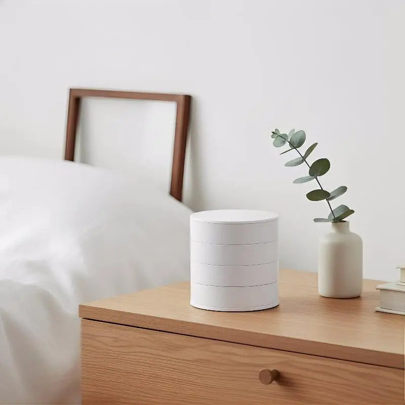 White cylindrical lamp on a wooden nightstand with a plant in the background