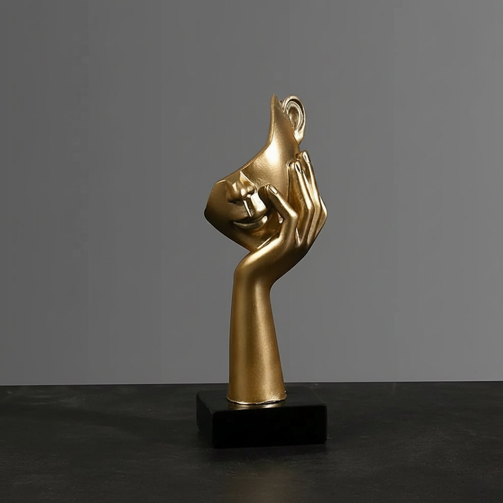 Gold sculpture of a hand covering a face with measurements on a dark surface and gray background