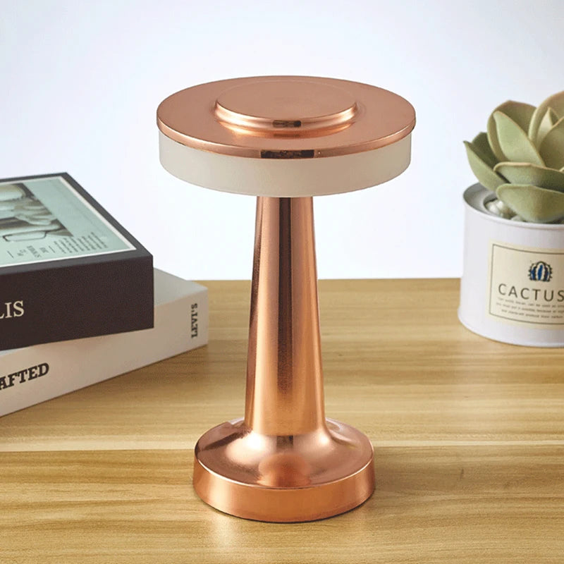 Copper-colored lamp on a wooden surface with books and a potted plant in the background