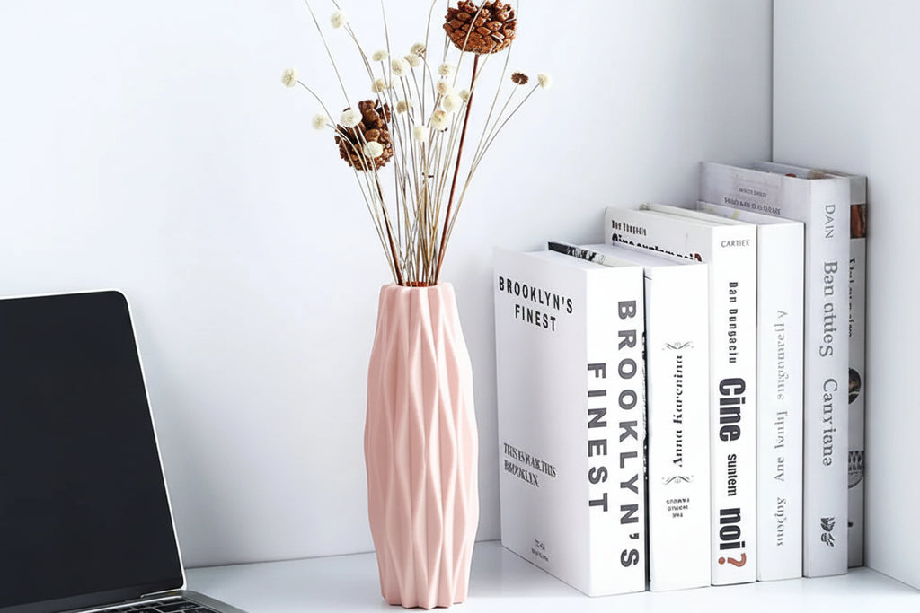 Pink vase with dried flowers on a white surface with books in the background