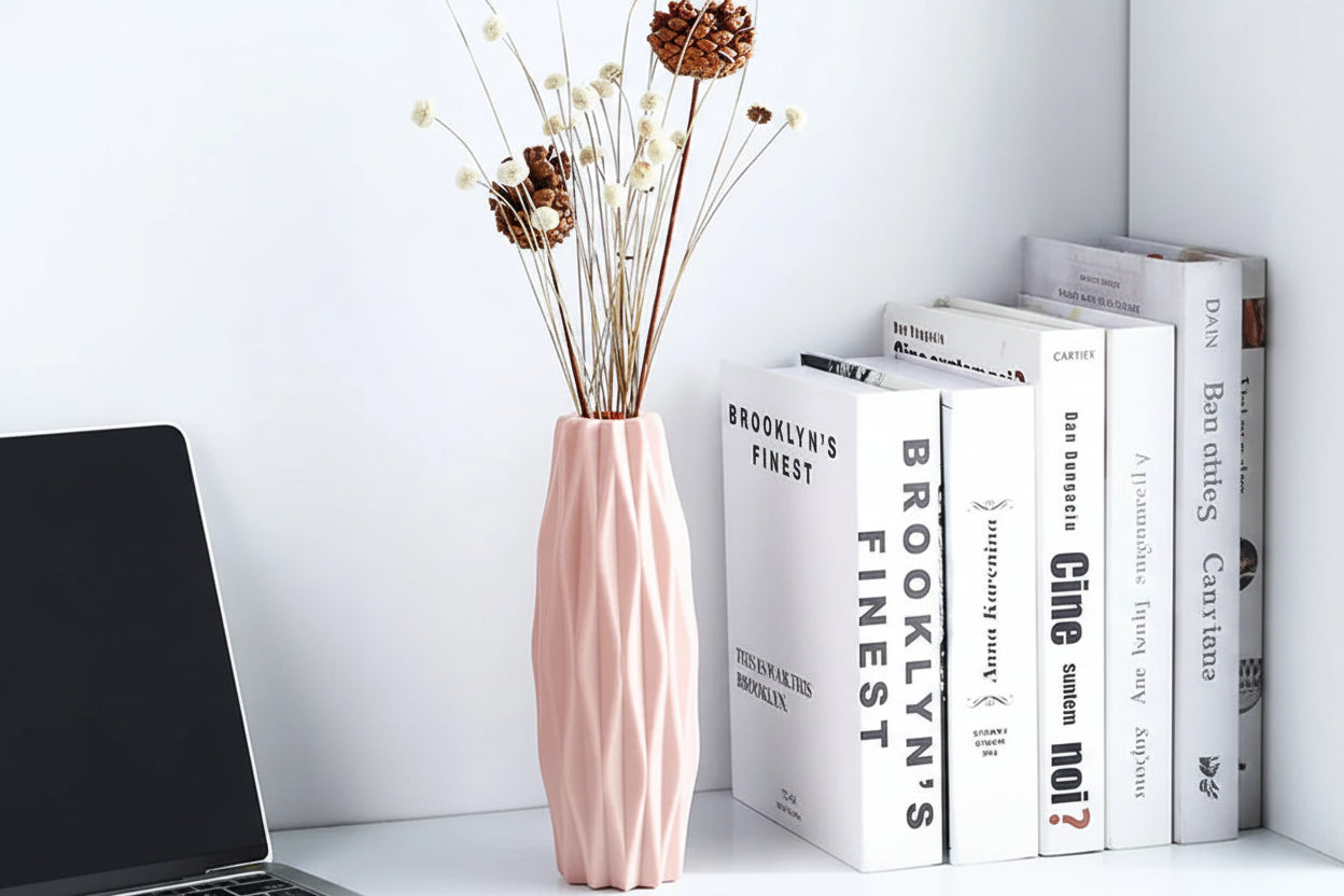 Pink vase with dried flowers on a white surface with books in the background
